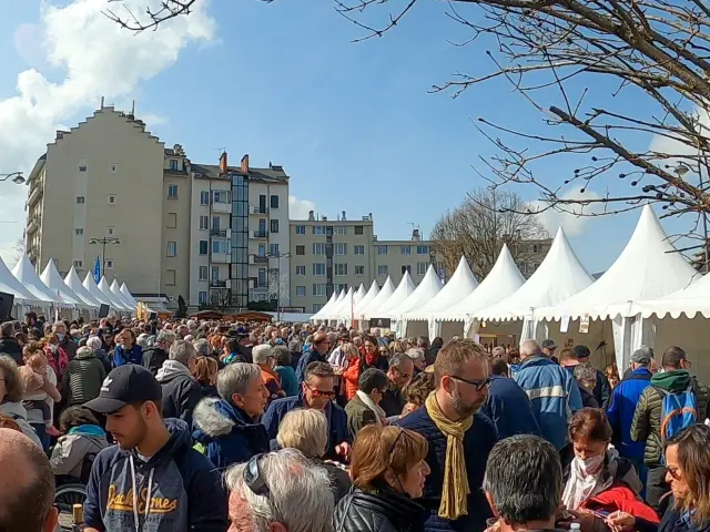 Grande tour circulaire avec des drapeaux en haut, entourée d’une foule nombreuse sous des structures blanches en forme de tente