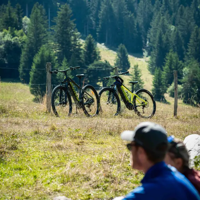 Deux personnes assises dans l’herbe, discutant près de leurs vélos posés au sol