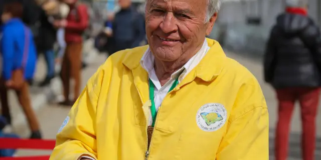 Homme âgé en tenue jaune avec un badge, tenant un téléphone, lors d’un événement sportif