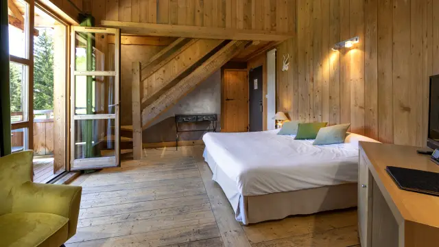 Camera d’albergo con letto matrimoniale, testiera in legno, comodino e finestra che affaccia su un balcone