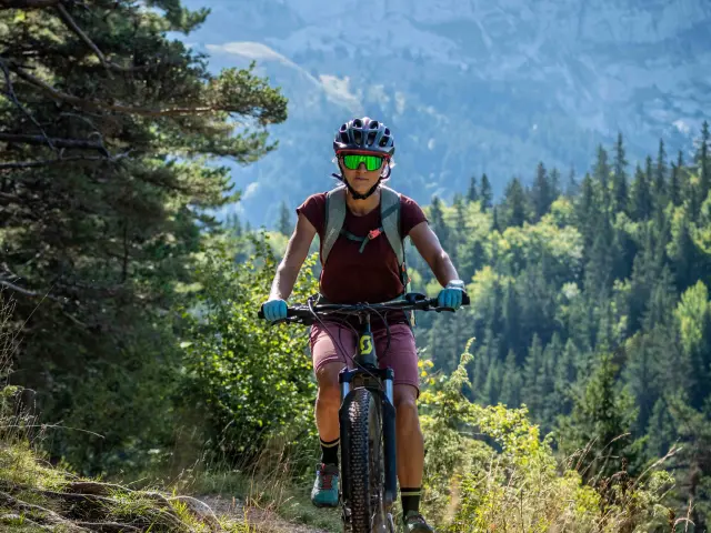 Cycliste portant un casque vert et un t-shirt rouge sur une route de montagne