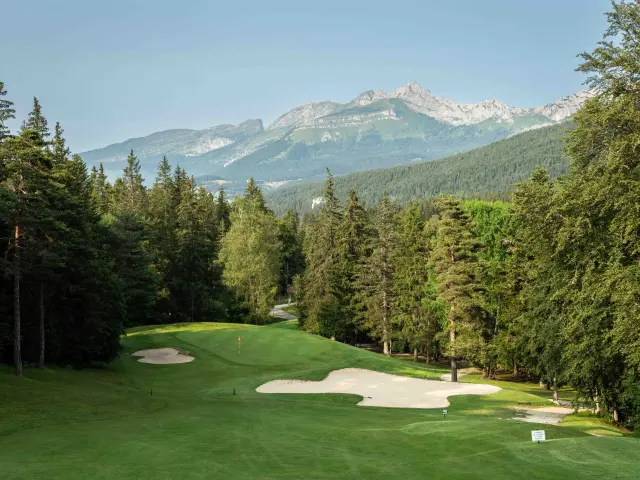 Parco paesaggistico con prati, alberi, panchine e montagne innevate sullo sfondo