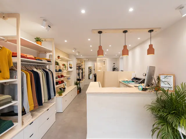 Interno di un caffè-boutique con scaffale di vestiti, bancone e piante verdi