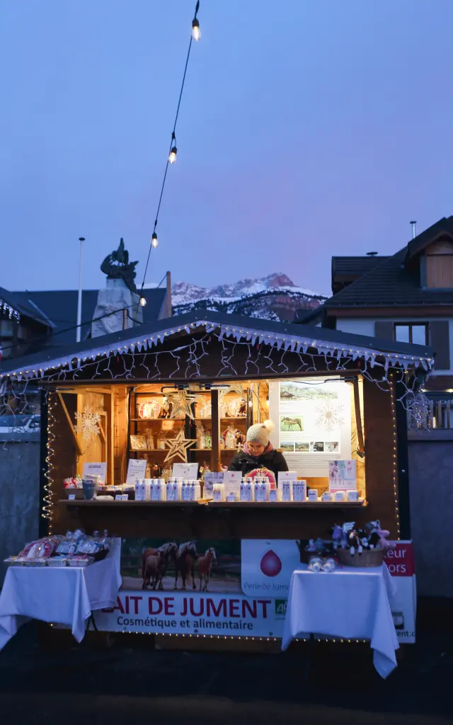 Bancarelle di mercato notturno illuminate da ghirlande luminose, con montagne sullo sfondo