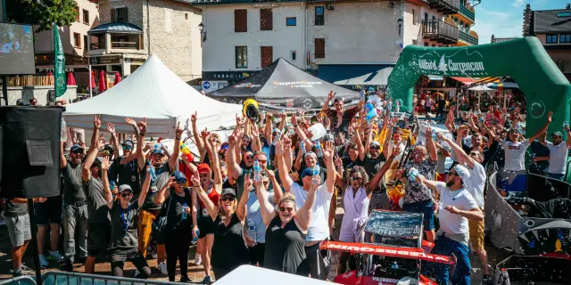 Gruppo di persone su un molo durante un evento festivo, con barche a vela ormeggiate sullo sfondo