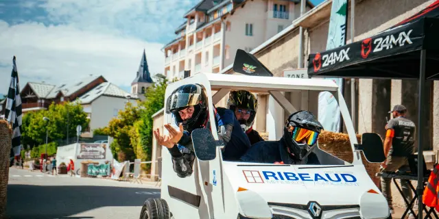 Sfilata di moto con piloti che indossano caschi e giacche, davanti a edifici e un'insegna ZAMX