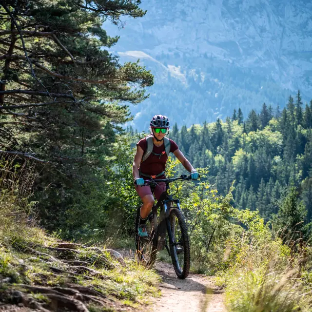 Cycliste en tenue rouge et casque à motifs colorés roulant sur un chemin de montagne ensoleillé