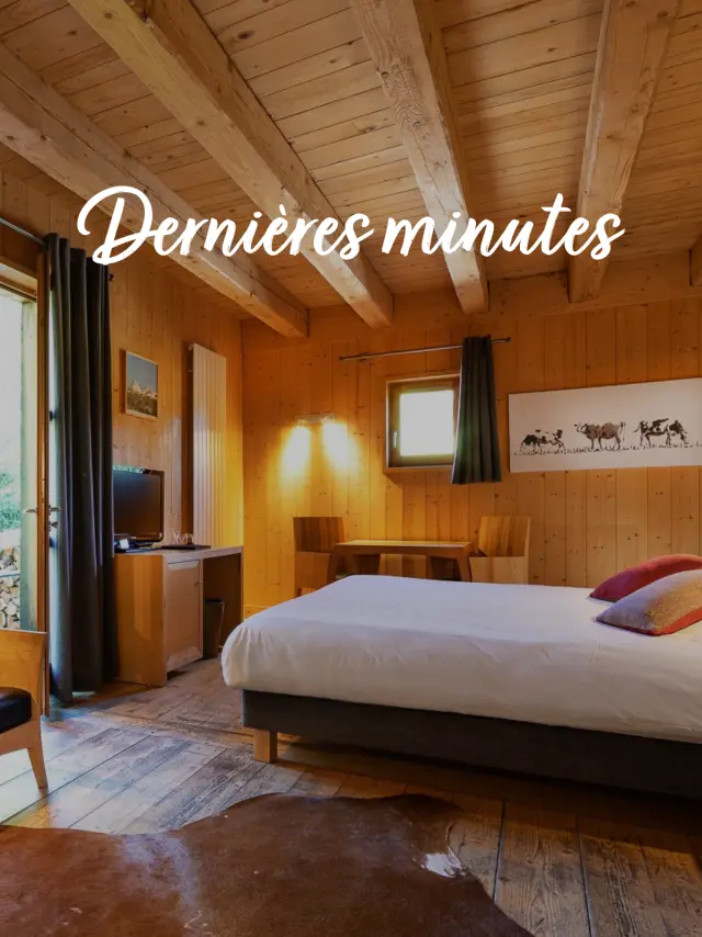 Camera d'albergo con letto matrimoniale, comodino, lampada e finestra che affaccia su un corridoio illuminato