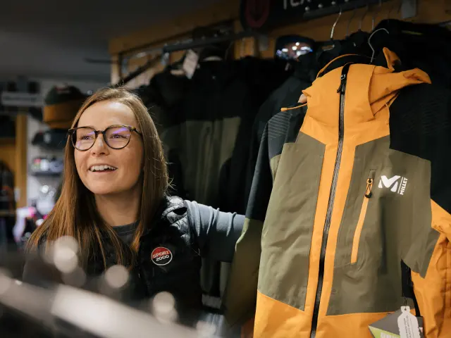 Femme portant des lunettes et un badge, tenant une guitare électrique jaune dans un magasin de musique