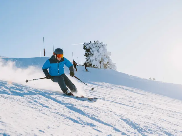 Skieur en tenue bleue et casque orange descendant une piste de ski enneigée