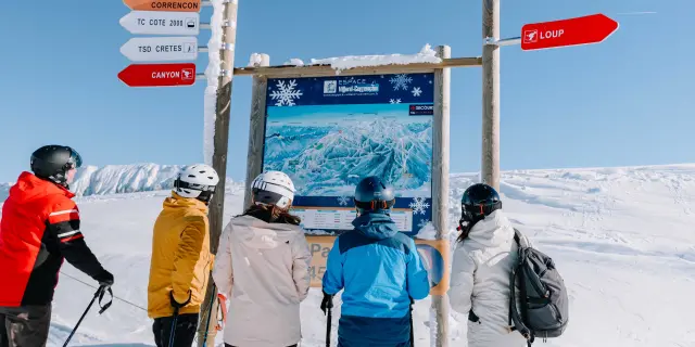 Gruppo di sciatori in abbigliamento invernale che parlano vicino a un cartello indicatore su una pista da sci