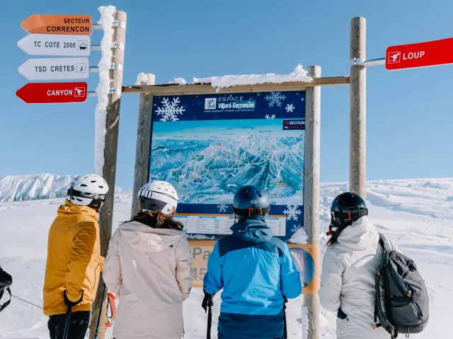 Groupe de skieurs en tenue hivernale discutant près d'un panneau indicateur sur une piste de ski