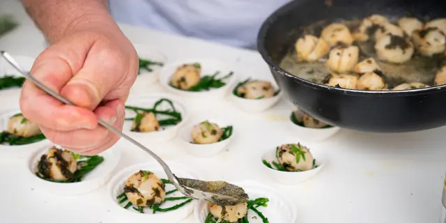 Mains tenant des rouleaux de sushi avec du riz, de l'avocat et des graines de sésame sur une planche en bois