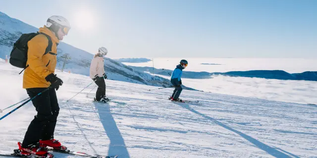 Tre sciatori su un ghiacciaio innevato, tra cui un bambino e due adulti, con bastoncini e sci