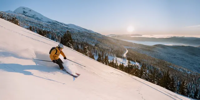 Sciatore in tuta gialla e casco blu che scende su una pista da sci innevata