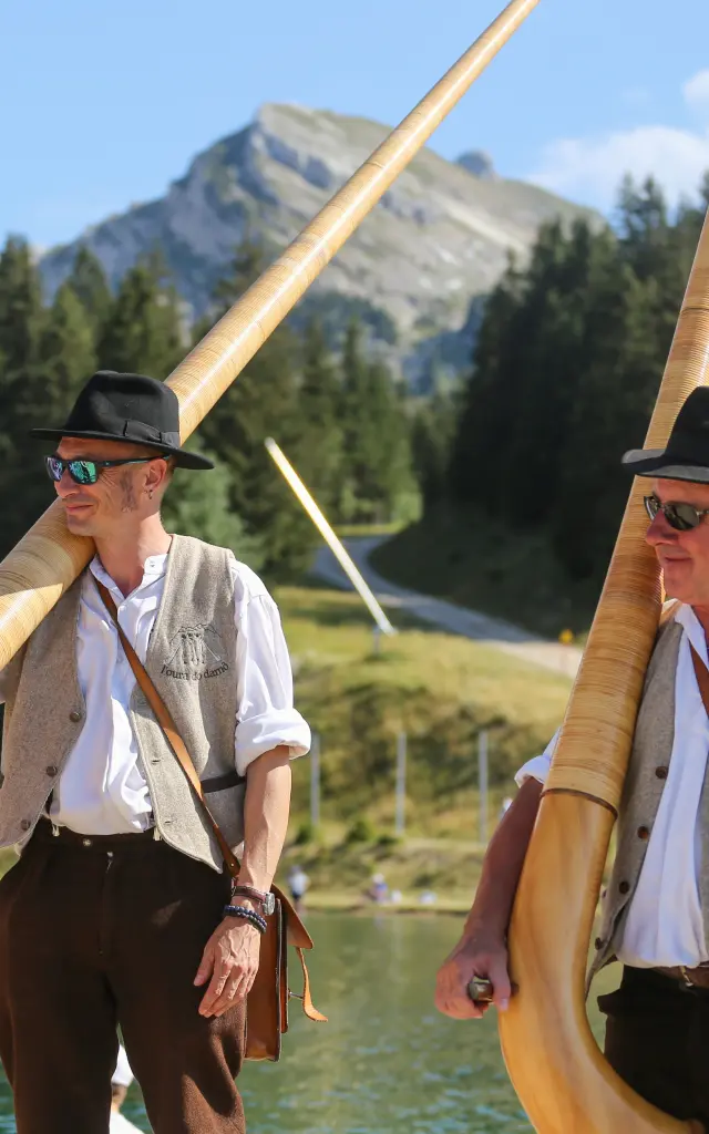 Due marinai in divisa bianca e berretto su una barca a vela, con montagne sullo sfondo