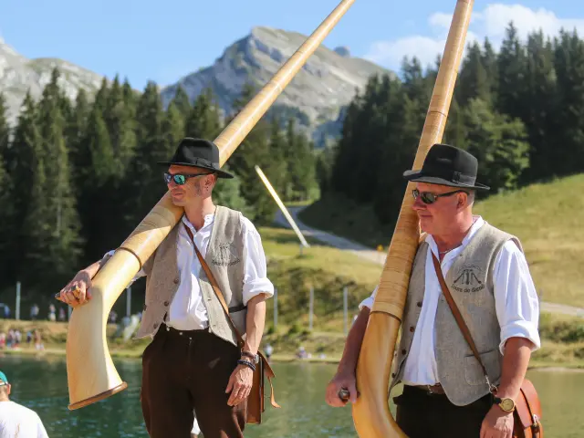 Due marinai in divisa bianca e berretto su una barca a vela, con montagne sullo sfondo