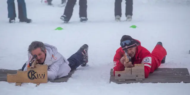 Deux enfants assis sur des luges colorées dans la neige, entourés d’adultes