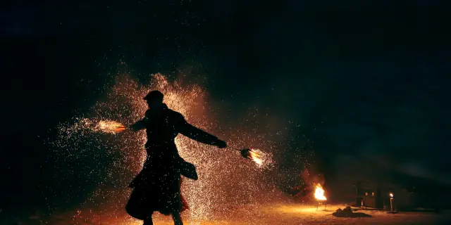 Personnes silhouettées devant un feu de camp près d’un plan d’eau au crépuscule