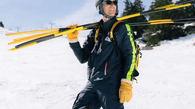 Sciatore in tenuta blu e gialla che scende una pista da sci con i bastoncini