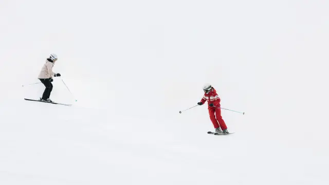 Due sciatori in abbigliamento da sci, uno in blu e bianco, l'altro in rosso, su una pista innevata