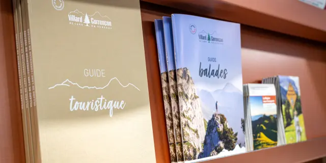 Due guide turistiche aperte in una vetrina di legno, con mappe e illustrazioni di paesaggi