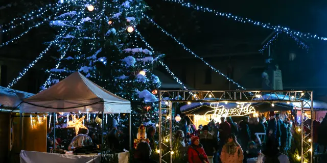 Night market with stalls lit by glowing garlands and pedestrians