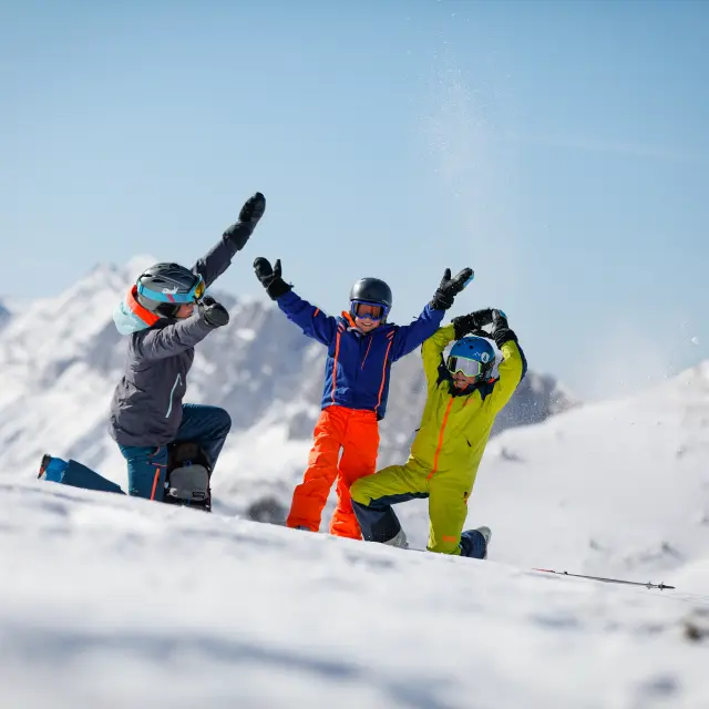Tre sciatori in abbigliamento colorato in piedi su un ghiacciaio con montagne sullo sfondo