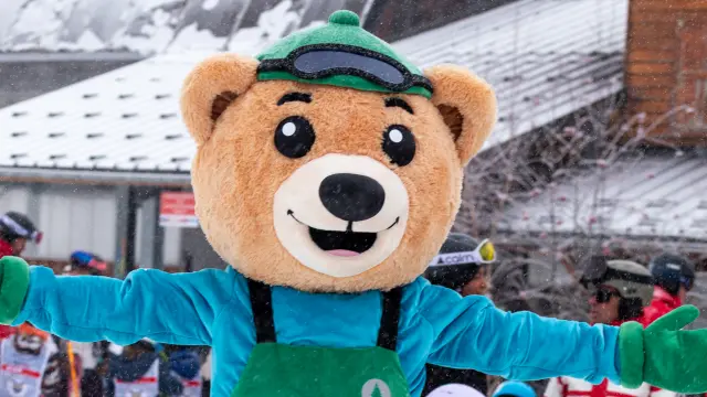 Personne déguisée en mascotte souriante avec un costume vert et bleu, patinant sur une piste glacée
