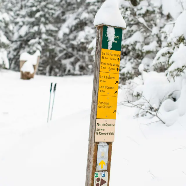 Panneau d'information en bois planté dans la neige, avec des pictogrammes et du texte en français