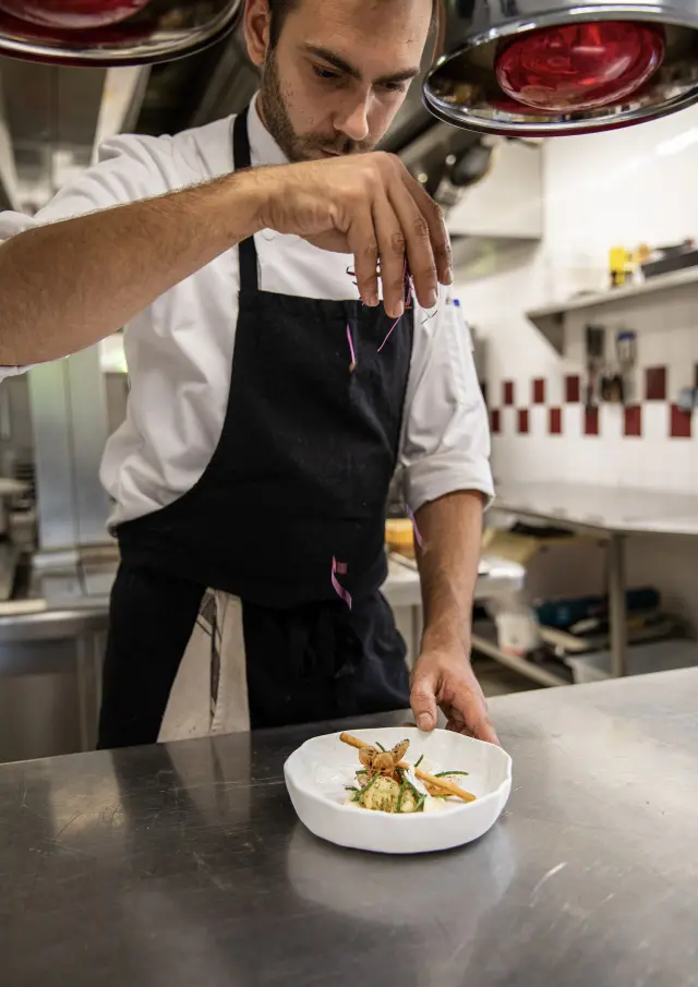 Chef en tablier noir préparant un plat avec des fleurs comestibles dans une cuisine professionnelle
