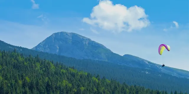 Colorful paraglider flying above a lake surrounded by mountains and forests