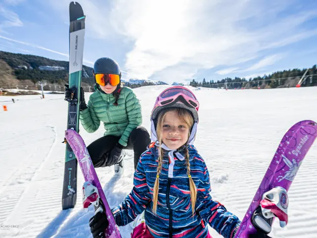 Deux enfants en tenue de ski, équipés de bâtons et de skis roses, sur une piste enneigée