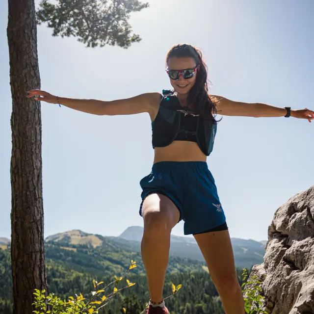 Donna in abbigliamento sportivo che tiene un ramo d'albero, in equilibrio su un altro ramo