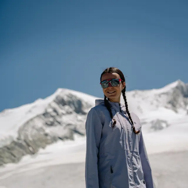 Donna in abbigliamento da escursionismo in piedi su un sentiero di montagna, con occhiali da sole e uno zaino