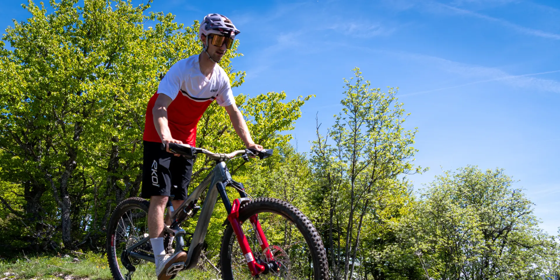Ciclista con casco e maglietta rossa che scende un sentiero boschivo in mountain bike