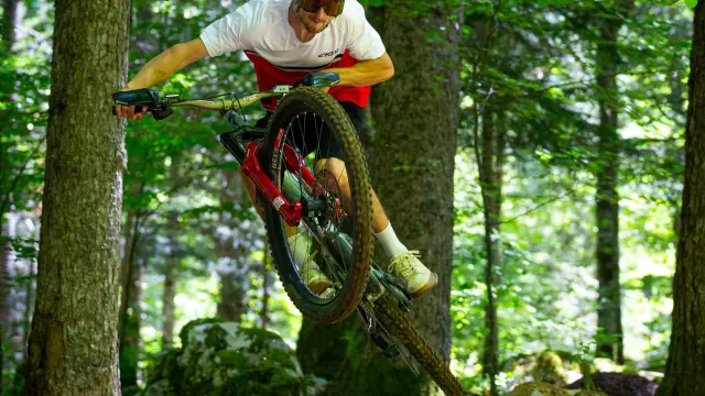 Motociclista con casco e tuta protettiva rossa e bianca, in discesa su un sentiero forestale in curva stretta