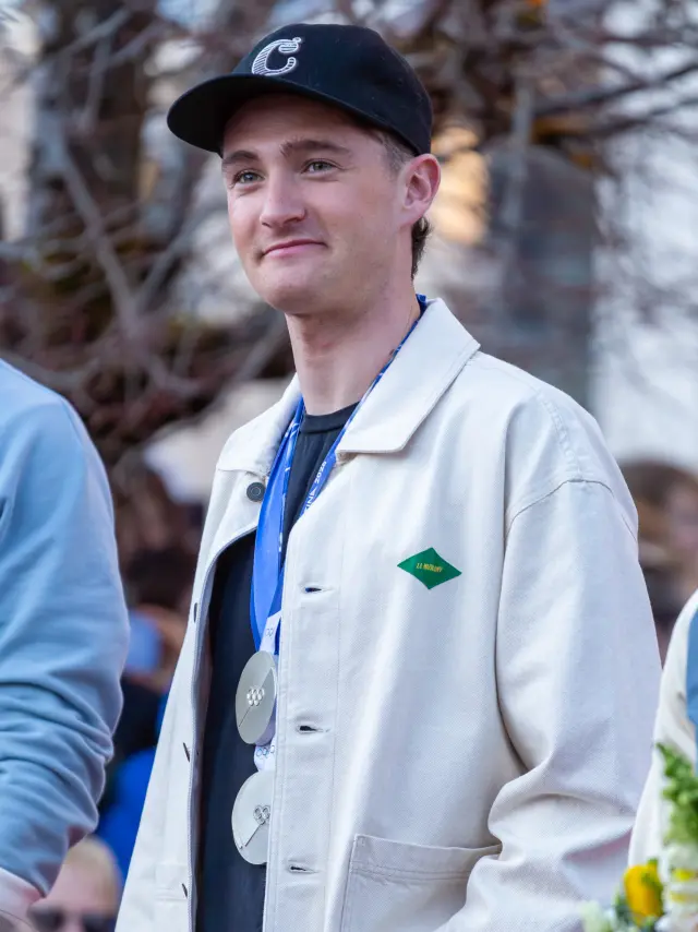 Uomo che indossa un completo bianco con cravatta blu e gilet a motivi, un cappello nero e una sciarpa a motivi, che tiene un bastone