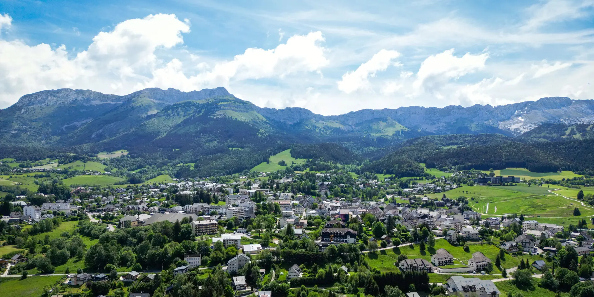 Village de montagne entouré de forêts et de montagnes, avec des maisons dispersées et une route sinueuse