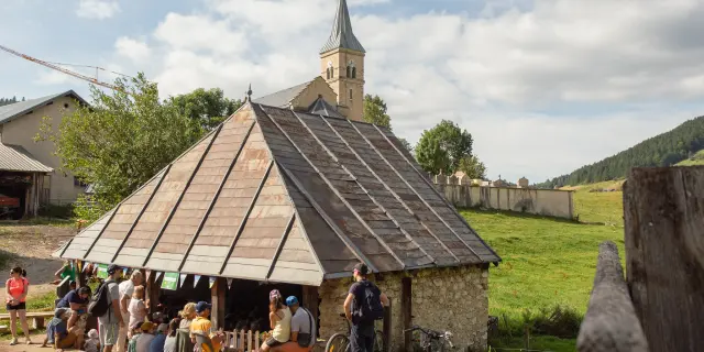 Marché artisanal en plein air avec des étals sous une halle à charpente apparente et une église gothique en arrière-plan